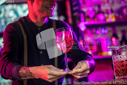 Image of Barman proposing alcoholic cocktails, shots, beverages to guest in multicolored neon light