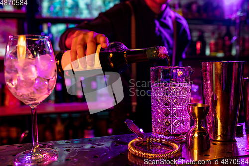 Image of Close up of barman finishes preparation of alcoholic cocktail, pouring drink in multicolored neon light