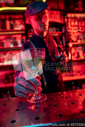 Image of Barman proposing alcoholic cocktails, shots, beverages to guest in multicolored neon light