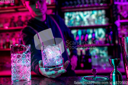 Image of Close up of barman finishes preparation of alcoholic cocktail in multicolored neon light