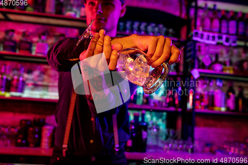 Image of Close up of barman finishes preparation of alcoholic cocktail, shaking ice in multicolored neon light