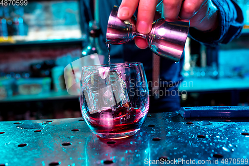 Image of Close up of barman preparing of alcoholic cocktail with shot in multicolored neon light