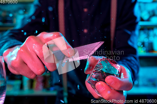 Image of Close up of barman crushing a big piece of ice on the bar counter with a special bar equipment on it for a cocktail