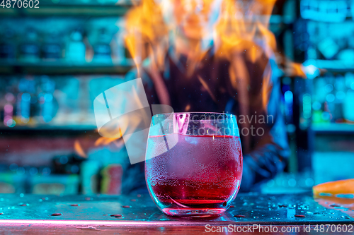 Image of Close up of alcoholic cocktail, beverage, drink in multicolored neon light with fire flames on the background