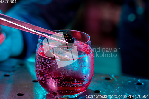 Image of Close up of barman decorating, preparing of alcoholic cold cocktail in multicolored neon light