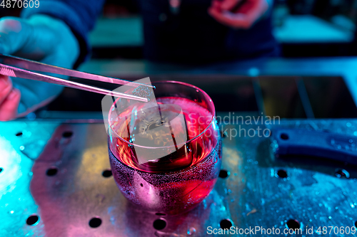 Image of Close up of barman decorating, preparing of alcoholic cold cocktail in multicolored neon light