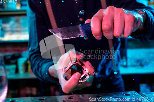 Image of Close up of barman crushing a big piece of ice on the bar counter with a special bar equipment on it for a cocktail