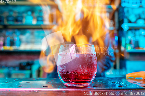 Image of Close up of alcoholic cocktail, beverage, drink in multicolored neon light with fire flames on the background