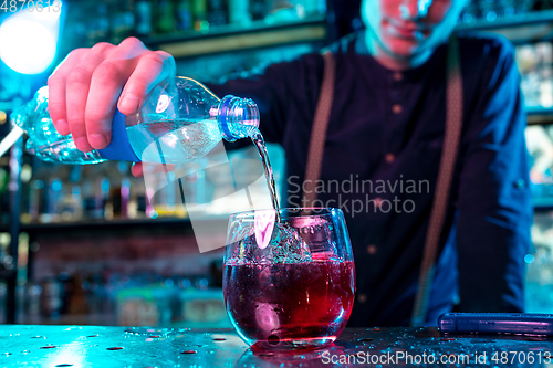 Image of Close up of barman decorating, preparing of alcoholic cold cocktail in multicolored neon light