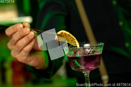 Image of Close up of barman finishes preparation of alcoholic cocktail in multicolored neon light