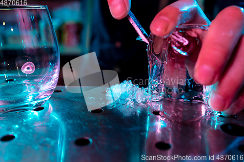 Image of Close up of barman crushing a big piece of ice on the bar counter with a special bar equipment on it for a cocktail