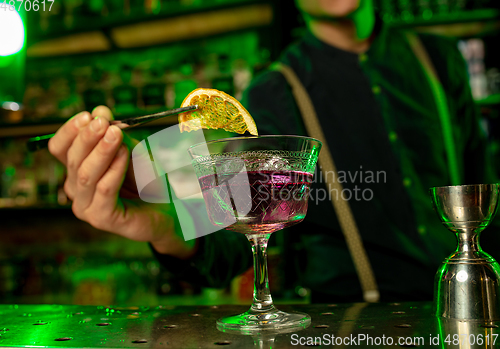 Image of Close up of barman finishes preparation of alcoholic cocktail in multicolored neon light