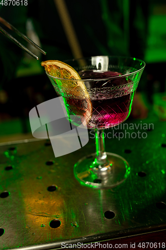 Image of Close up of barman finishes preparation of alcoholic cocktail in multicolored neon light