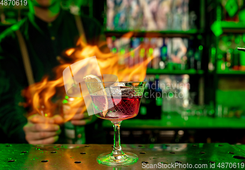 Image of Close up of alcoholic cocktail, beverage, drink in multicolored neon light with fire flames on the background