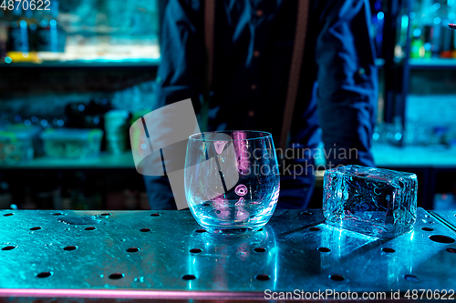 Image of Close up of huge ice cube and drinking glass in multicolored neon light at bar