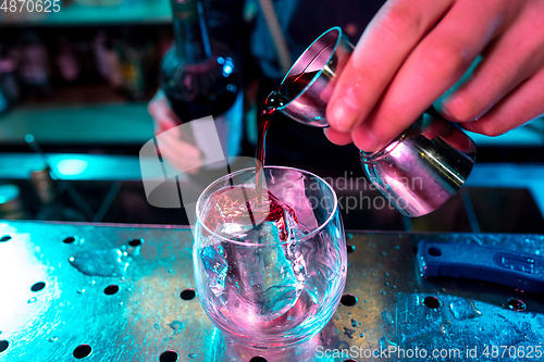 Image of Close up of barman preparing of alcoholic cocktail with shot in multicolored neon light