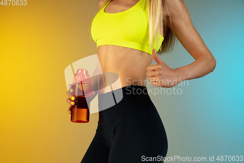 Image of Close up of young and sportive woman with fit belly and well-kept skin holding red water bottle on gradient background. Perfect body ready for summertime.
