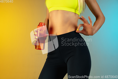 Image of Close up of young and sportive woman with fit belly and well-kept skin holding red water bottle on gradient background. Perfect body ready for summertime.