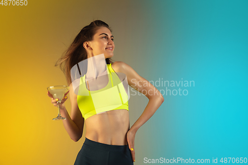 Image of Fashion portrait of young fit and sportive woman drinking cocktail on gradient background. Perfect body ready for summertime.