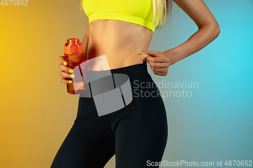 Image of Close up of young and sportive woman with fit belly and well-kept skin holding red water bottle on gradient background. Perfect body ready for summertime.