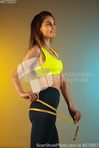 Image of Fashion portrait of young fit and sportive woman with measurer on gradient background. Perfect body ready for summertime.