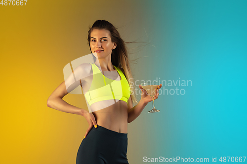 Image of Fashion portrait of young fit and sportive woman drinking cocktail on gradient background. Perfect body ready for summertime.