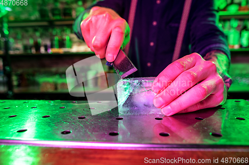 Image of Close up of barman crushing a big piece of ice on the bar counter with a special bar equipment on it for a cocktail