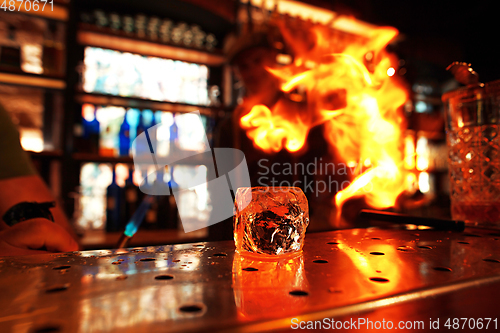 Image of Close up big melting piece of ice on the bar counter in fireflames on it, preparation for a cocktail