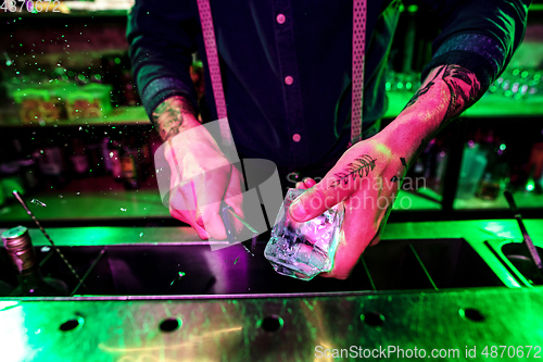 Image of Close up of barman crushing a big piece of ice on the bar counter with a special bar equipment on it for a cocktail