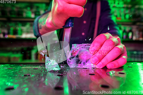 Image of Close up of barman crushing a big piece of ice on the bar counter with a special bar equipment on it for a cocktail