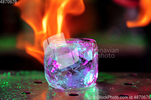 Image of Close up big melting piece of ice on the bar counter in fireflames on it, preparation for a cocktail