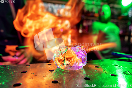 Image of Close up big melting piece of ice on the bar counter in fireflames on it, preparation for a cocktail