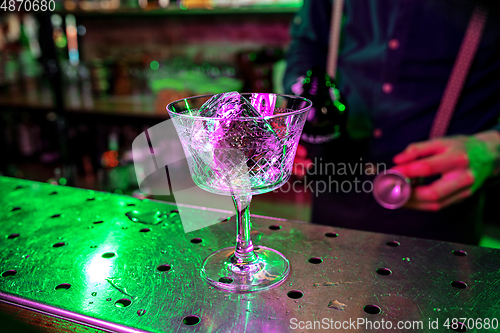 Image of Close up of barman finishes preparation of alcoholic cocktail, pouring drink with shot in multicolored neon light, focus on glass