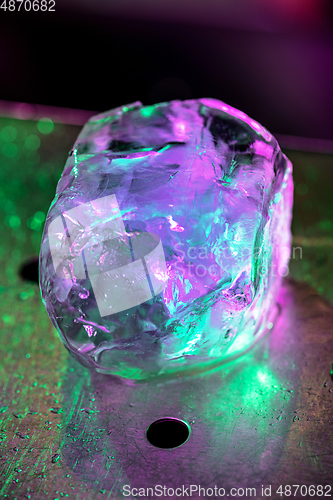 Image of Close up big melting piece of ice on the bar counter in pink-green neon light on it, preparation for a cocktail