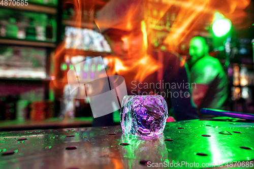 Image of Close up big melting piece of ice on the bar counter in fireflames on it, preparation for a cocktail