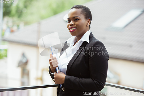 Image of African-american businesswoman in office attire smiling, looks confident and happy, successful