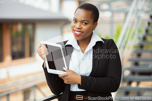 Image of African-american businesswoman in office attire smiling, looks confident and happy, successful