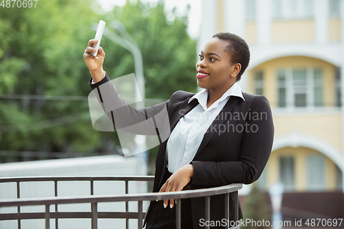 Image of African-american businesswoman in office attire smiling, looks confident and happy, successful