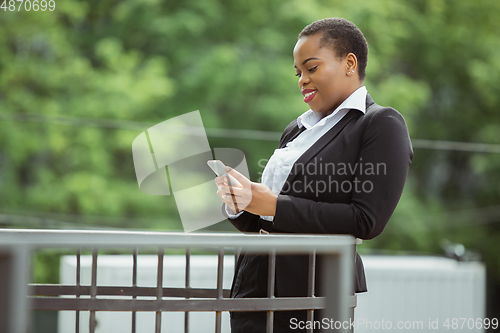 Image of African-american businesswoman in office attire smiling, looks confident and happy, successful