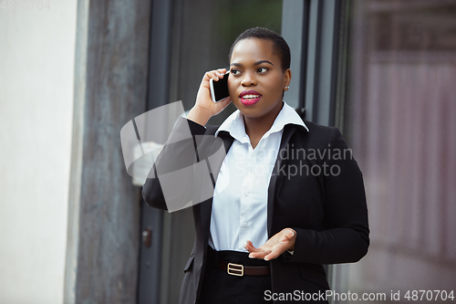 Image of African-american businesswoman in office attire smiling, looks confident and happy, successful