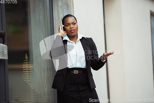 Image of African-american businesswoman in office attire smiling, looks confident and happy, successful