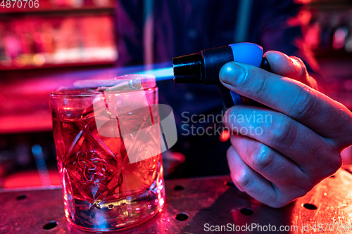 Image of Close up of alcoholic cocktail, beverage, drink in multicolored neon light with fire flame setting on top
