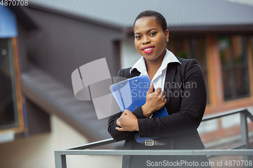 Image of African-american businesswoman in office attire smiling, looks confident and happy, successful