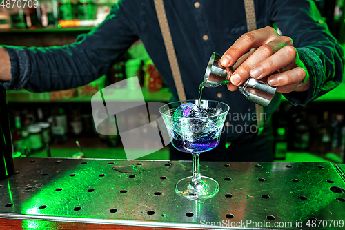 Image of Close up of barman finishes preparation of alcoholic cocktail, pouring drink with shot in multicolored neon light, focus on glass