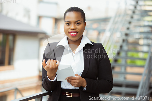 Image of African-american businesswoman in office attire smiling, looks confident and happy, successful