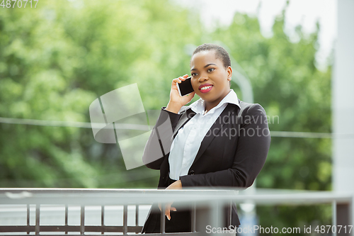 Image of African-american businesswoman in office attire smiling, looks confident and happy, successful