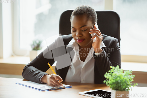 Image of African-american businesswoman in office attire smiling, looks confident and happy, successful