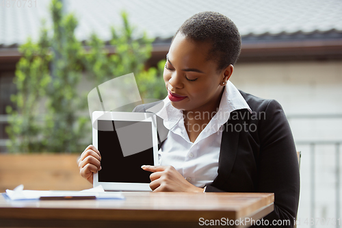 Image of African-american businesswoman in office attire smiling, looks confident and happy, successful