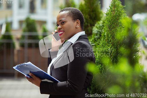 Image of African-american businesswoman in office attire smiling, looks confident and happy, successful