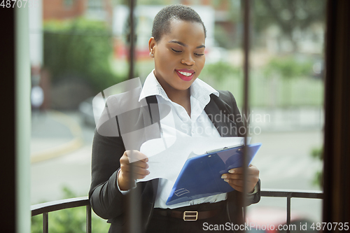 Image of African-american businesswoman in office attire smiling, looks confident and happy, successful